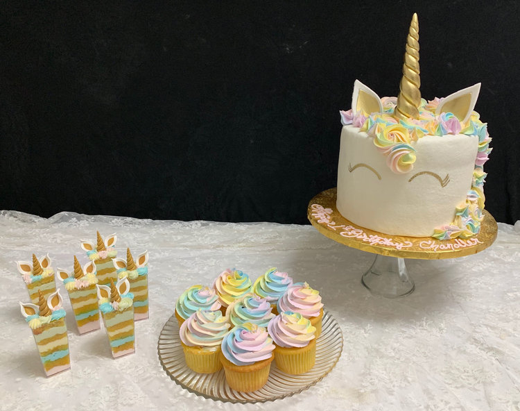 Unicorn-inspired cake, cupcakes and sliced cake on top of a white table linen 