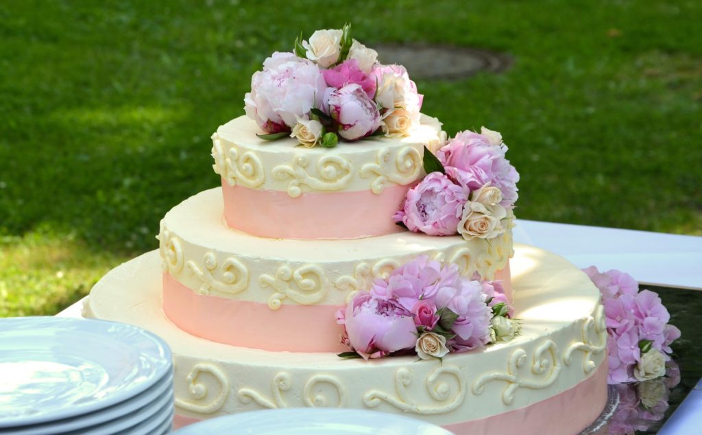 how to charge for cake delivery - A pink and white wedding cake on a table outside.